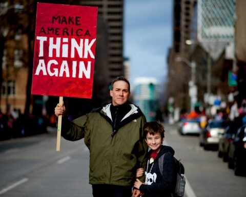 man beside boy holding red and white rally signage