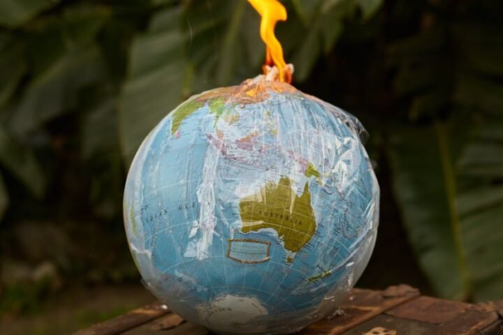 Environment ecology pollution concept burning Earth globe covered in transparent plastic bag in shape of bomb placed on wooden bench near green plants