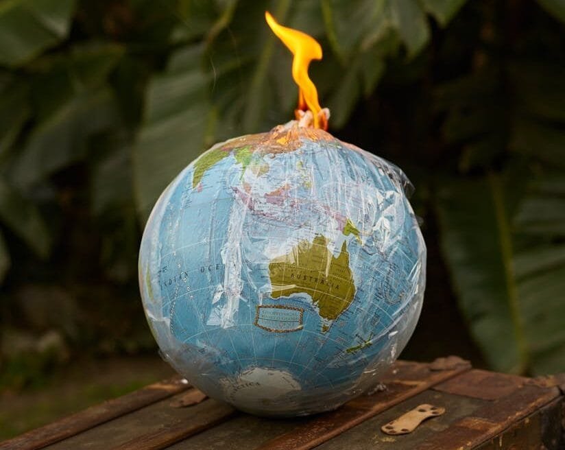 Environment ecology pollution concept burning Earth globe covered in transparent plastic bag in shape of bomb placed on wooden bench near green plants