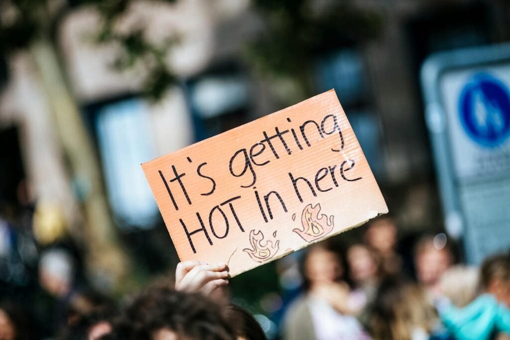 Hand holding a "It's getting hot in here" sign at a climate protest, emphasizing global warming.