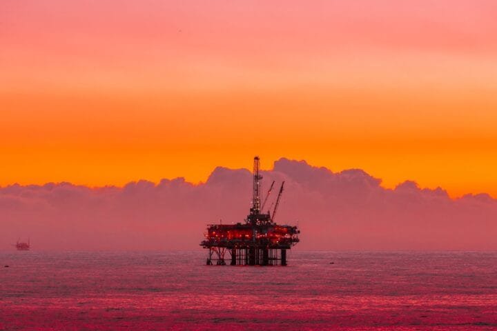 an oil rig in the middle of the ocean at sunset