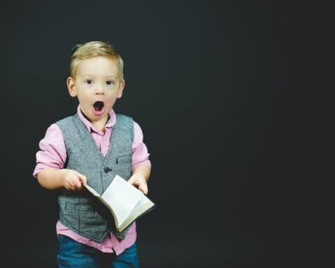 boy wearing gray vest and pink dress shirt holding book